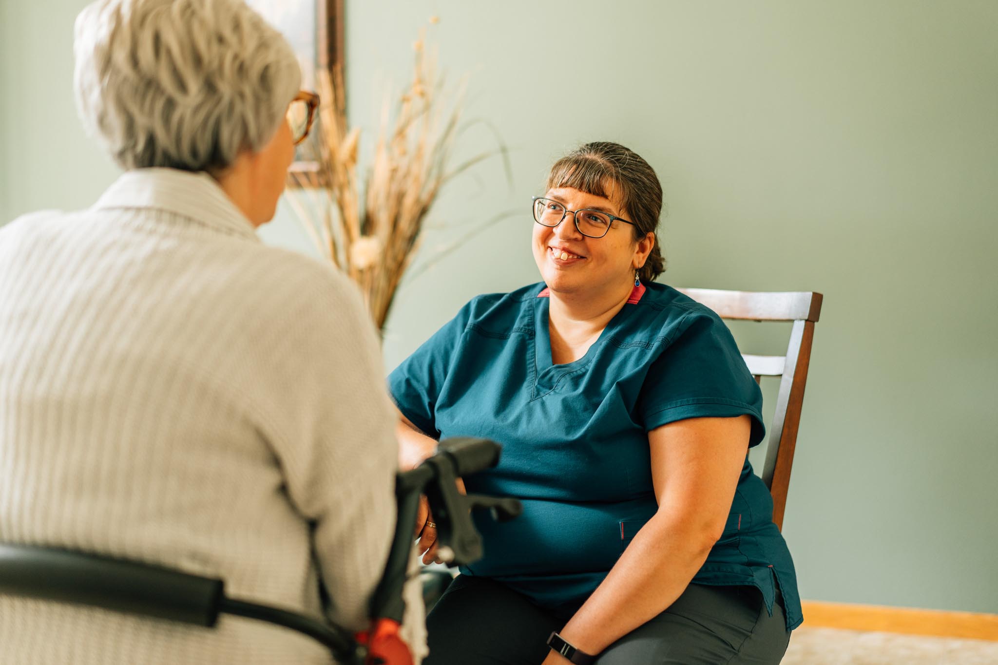 A nurse sits in front of an elderly patient while smiling at her.