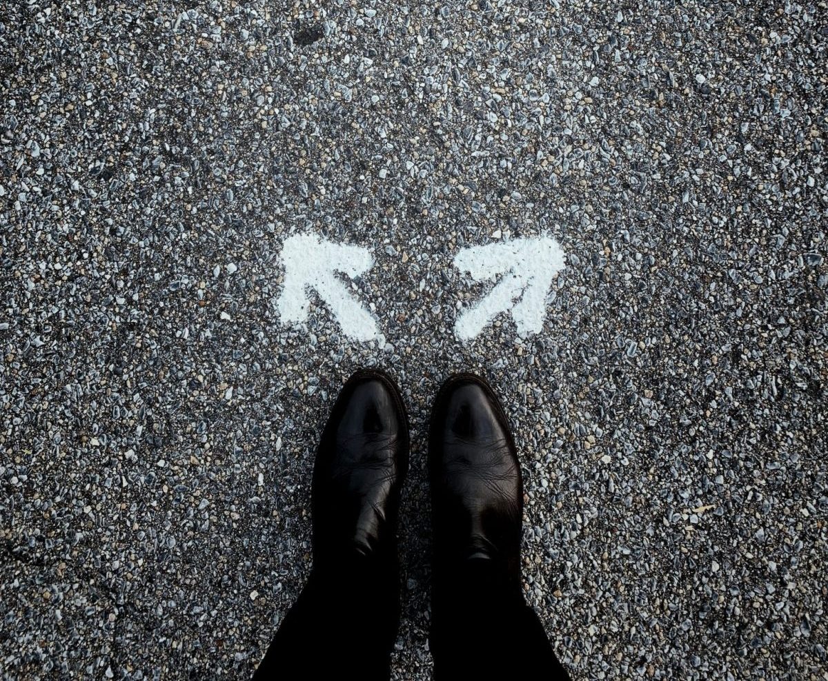 Person in black dress pants and shoes looking for jobs for teachers changing careers and standing above two arrows spray painted on street